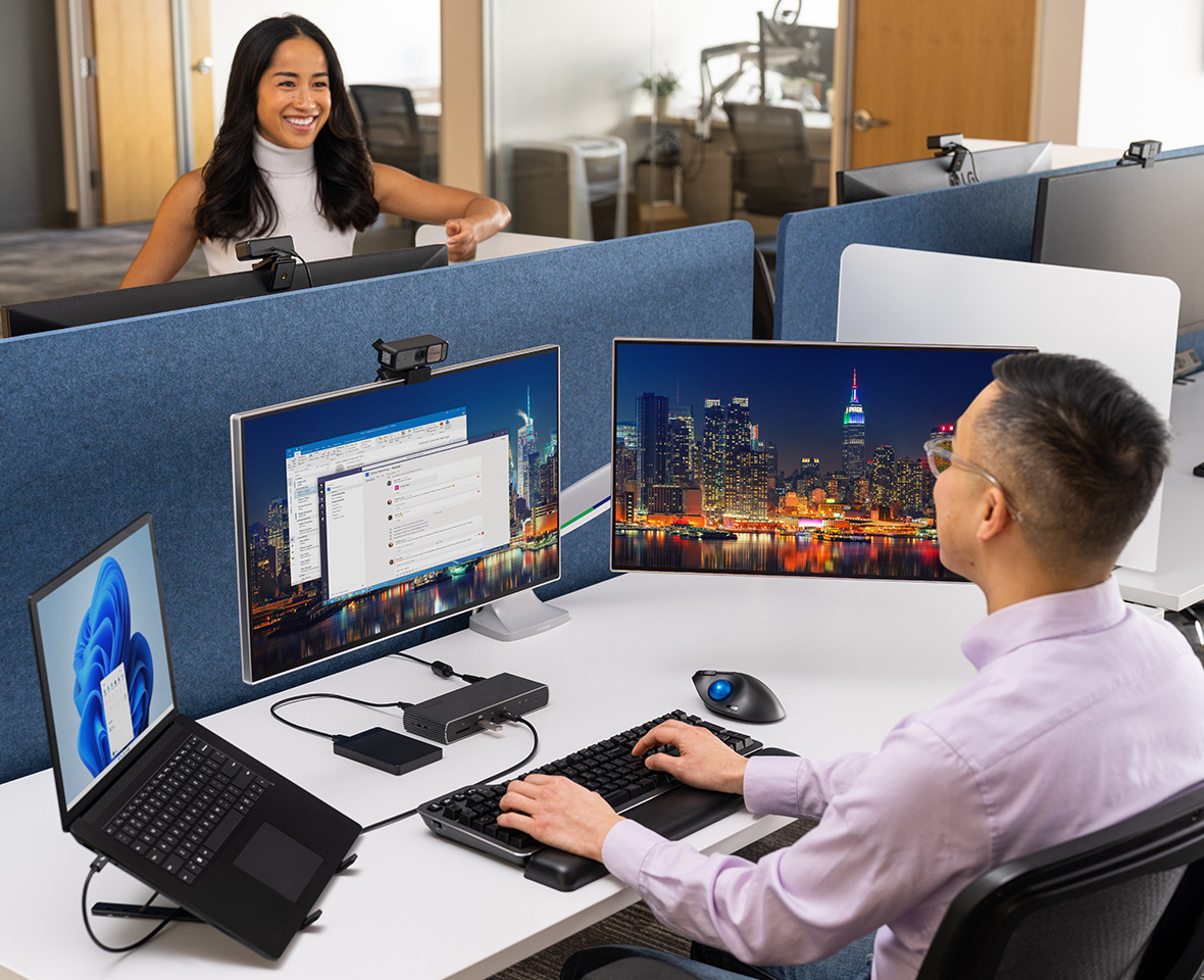 A woman talking to a man who is working at his desk with Kensington computer accessories