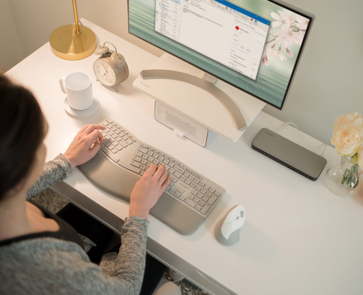 Woman typing on ergonomic keyboard at desk at home.