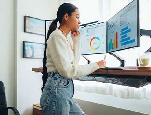 Woman working at standing desk with 2 monitors.